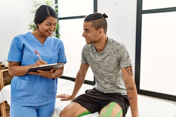 Young latin physioterapist woman asking to patient at the clinic.