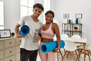 Fototapeta na wymiar Young latin sporty couple smiling happy holding yoga mat and bottle ofa water at home