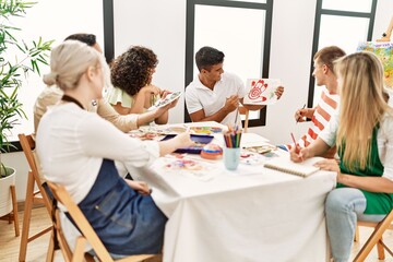 Group of people smiling happy drawing sitting on the table at art studio.