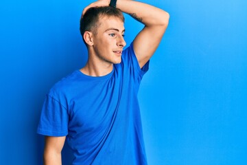 Young caucasian man wearing casual blue t shirt smiling confident touching hair with hand up gesture, posing attractive and fashionable