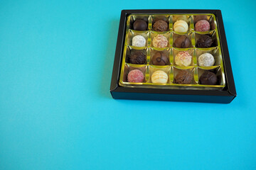 many different round chocolate truffles lie in a box on a blue background. side view.  high-calorie sweets. copy space