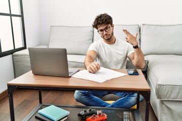 Fototapeta premium Hispanic man doing papers at home shooting and killing oneself pointing hand and fingers to head like gun, suicide gesture.