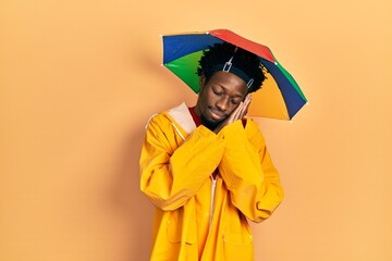 Young african american man wearing yellow raincoat sleeping tired dreaming and posing with hands together while smiling with closed eyes.