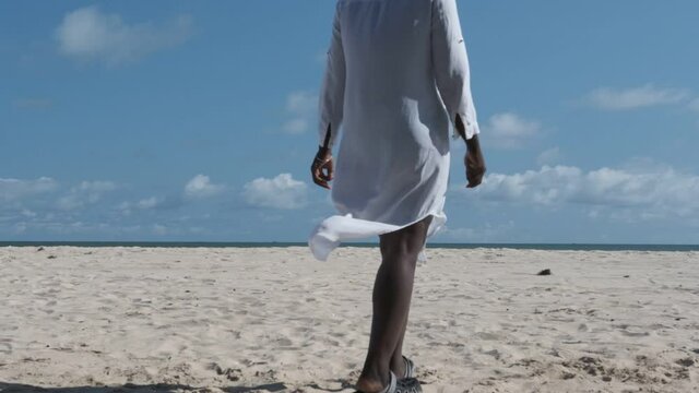 African woman in shirt and hat walking down to the sea in bojo beach Accra Ghana West Africa