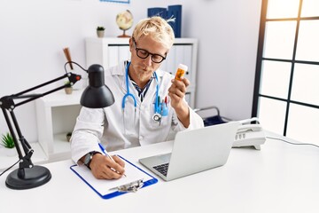 Young caucasian man wearing doctor uniform holding pills at clinic