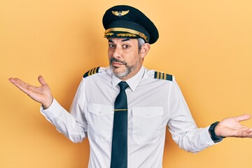 Handsome middle age man with grey hair wearing airplane pilot uniform clueless and confused expression with arms and hands raised. doubt concept.