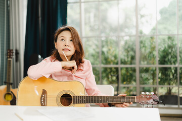 Asian girl is learning to play the guitar online at home. A female musician plays a song while...