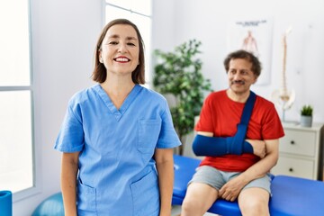 Obraz premium Middle age doctor woman with patient with arm injury at rehabilitation clinic with a happy and cool smile on face. lucky person.
