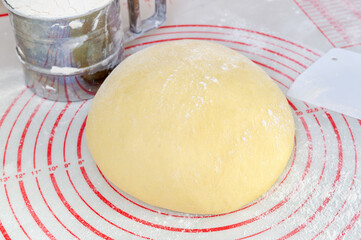 Raw yeast dough on the floured silicone baking mat with markings on the kitchen table.