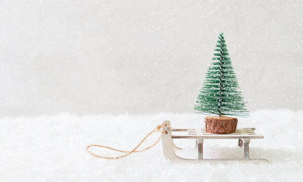 Beautiful winter minimalistic postcard. Toy fir tree on a sled on a snowy background. Concept for Christmas holidays, gift delivery. Copy space.