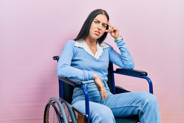 Beautiful woman with blue eyes sitting on wheelchair worried and stressed about a problem with hand...