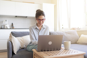 Smiling young woman freelancer with laptop communicating with client via video call. Pleasant professional female tutor giving language class at home office distantly. Distance webinar online teaching