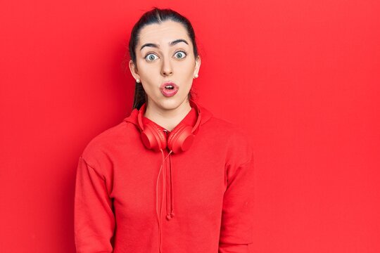 Beautiful woman with blue eyes wearing gym clothes and headphones scared and amazed with open mouth for surprise, disbelief face