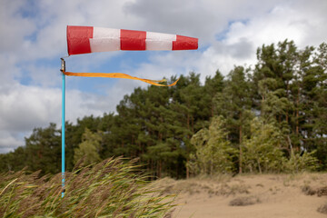 Windsock on a sandy beach in strong wind, Red and white fabric cone designed to indicate the...