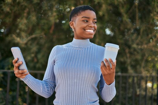 Young african american woman using smartphone and drinking coffee at the city