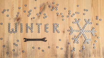 Word winter and a snowflake are lined with metal nuts on table, next to a wrench. New Year and Christmas holiday wait concept. 