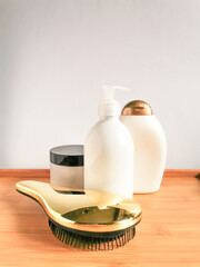 Bottles of shampoo and conditioner, golden hair brush and jar of hair mask on the wooden table.