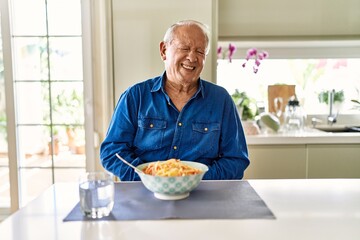 Senior man with grey hair eating pasta spaghetti at home with hand on stomach because indigestion, painful illness feeling unwell. ache concept.