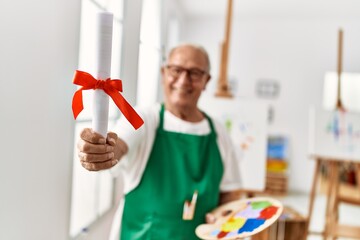 Senior grey-haired artist man smiling happy holding diplom at art studio.