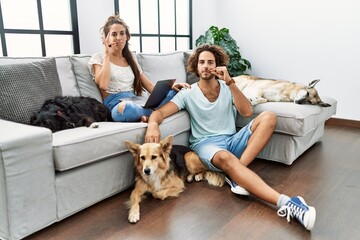 Young hispanic couple with dogs relaxing at home mouth and lips shut as zip with fingers. secret and silent, taboo talking