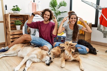 Young hispanic couple doing laundry with dogs smiling pointing to head with both hands finger, great idea or thought, good memory