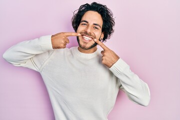 Handsome hispanic man wearing casual white sweater smiling cheerful showing and pointing with fingers teeth and mouth. dental health concept.