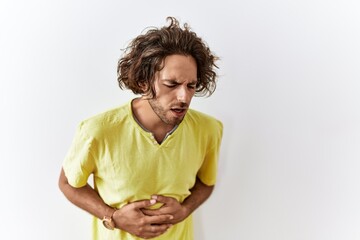 Young hispanic man standing over isolated background with hand on stomach because indigestion,...