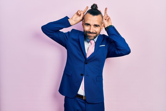 Young hispanic man wearing business suit and tie posing funny and crazy with fingers on head as bunny ears, smiling cheerful