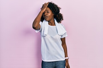 Young african american woman wearing sportswear and towel surprised with hand on head for mistake,...