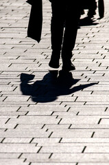 Schatten eines Menschen mit Einkaufstasche auf Straßenpflaster