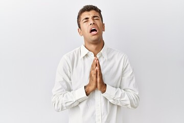 Young handsome hispanic man standing over isolated background begging and praying with hands together with hope expression on face very emotional and worried. begging.