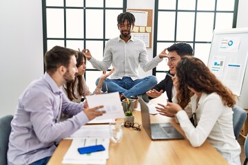 Businessman enjoys meditating during meeting. Sitting on desk near arguing partners at the office.