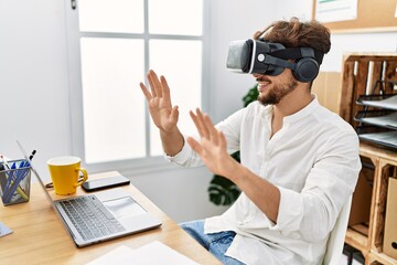Young arab man using vr goggles doing guitar gesture at office