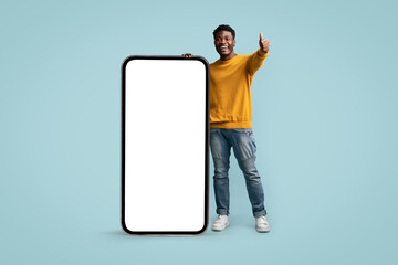 Positive black guy posing with big smartphone, showing thumb up