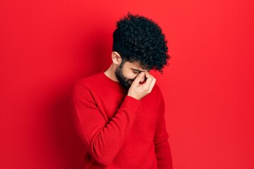 Fototapeta na wymiar Young arab man with beard wearing casual red sweater tired rubbing nose and eyes feeling fatigue and headache. stress and frustration concept.