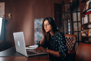 Young woman in glasses works at the laptop while sitting at table