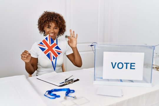 Young african american woman at political campaign election holding uk flag doing ok sign with fingers, smiling friendly gesturing excellent symbol