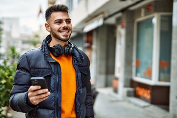 Handsome hispanic man with beard smiling happy and confident at the city wearing winter coat using smartphone