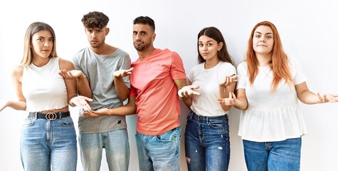 Group of young friends standing together over isolated background clueless and confused with open...