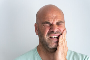 Close-up of bald, bearded Caucasian man gesturing a toothache.