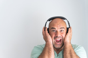 Face of a bald and bearded Caucasian man, wearing headphones, listening to music excitedly and gesturing with his hands.