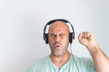 Face of a bald and bearded Caucasian man, wearing headphones, listening to music excitedly and gesturing with his hands.