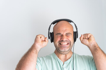Face of a bald and bearded Caucasian man, wearing headphones, listening to music excitedly and gesturing with his hands.