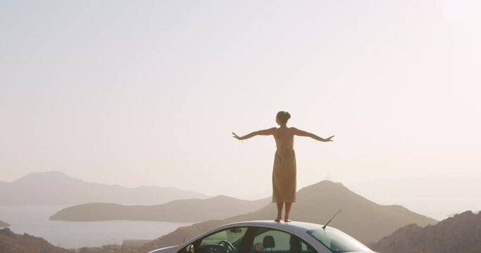 Young woman on road side on top of mountain and raises arms into air, waves his arms like a bird in fornt of sea landscape. Road adventures and happy holdays concept.