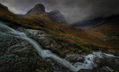 Dark and Moody image of Glencoe, Highlands Scotland with stream running off mountain. - obrazy, fototapety, plakaty