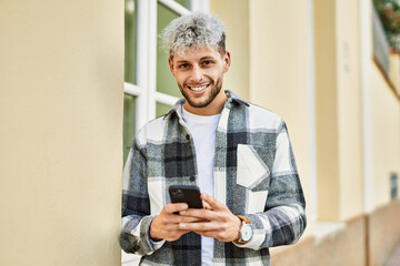 Fototapeta premium Young hispanic man smiling happy using smartphone at the city.