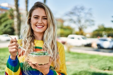 Fototapeta premium Young blonde woman eating healthy salad at the park