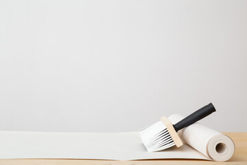 Brush and roll of wallpaper on wooden table at light gray wall background. Closeup. Repair work of...