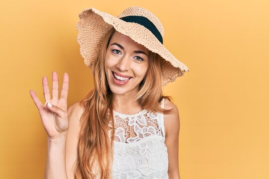 Young caucasian woman wearing summer hat showing and pointing up with fingers number four while smiling confident and happy.