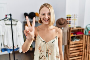 Obraz na płótnie Canvas Young caucasian woman at retail shop showing and pointing up with fingers number two while smiling confident and happy.